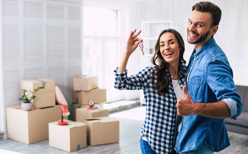 Happy couple in their new home, with unpacked boxes behind them