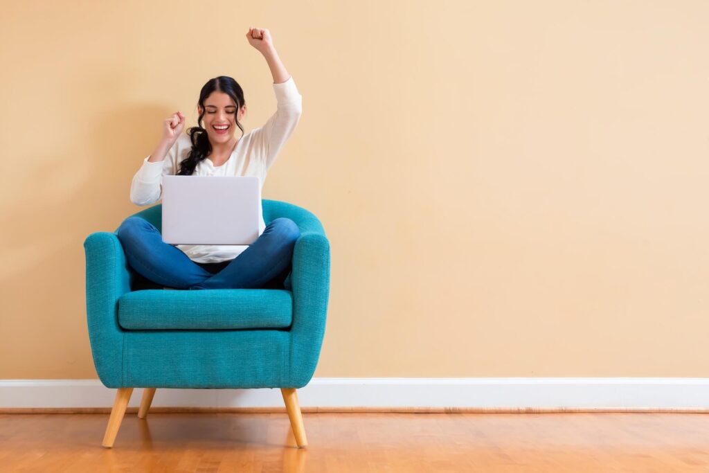 A happy woman sitting on an armchair with a laptop in her lap