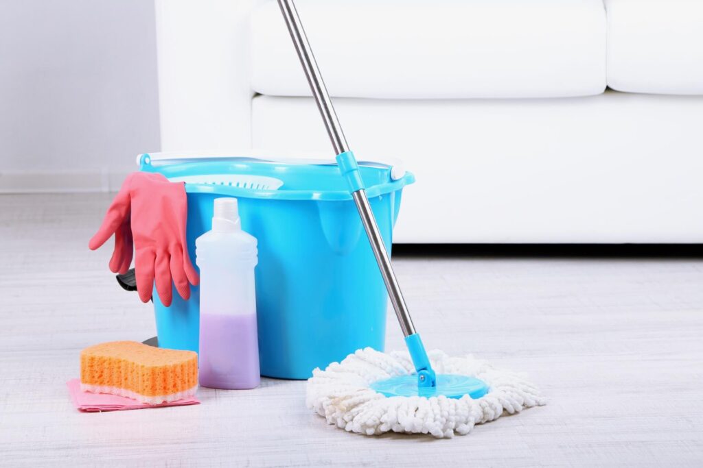 Cleaning supplies and a bucket on the floor next to a white sofa   