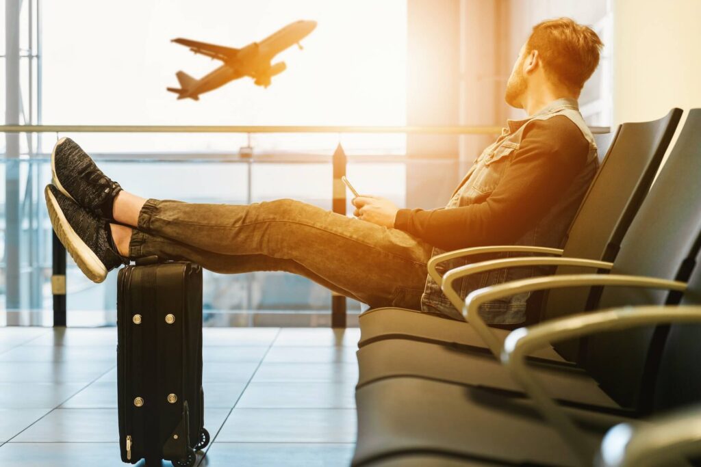 Man sitting at the airport holding his legs on the suitcase  