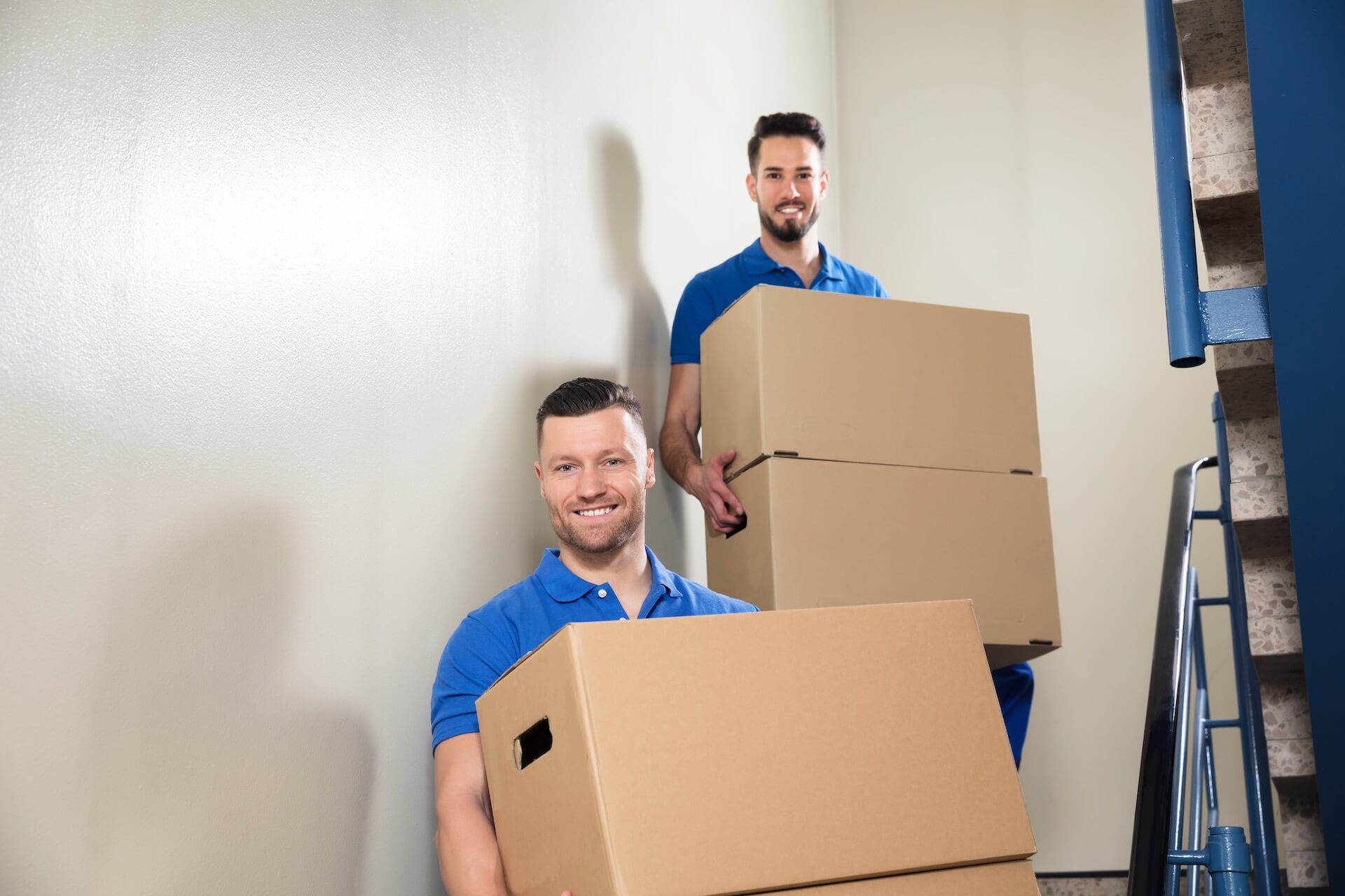 Two international movers in blue shirts, standing on the stairs and holding packages