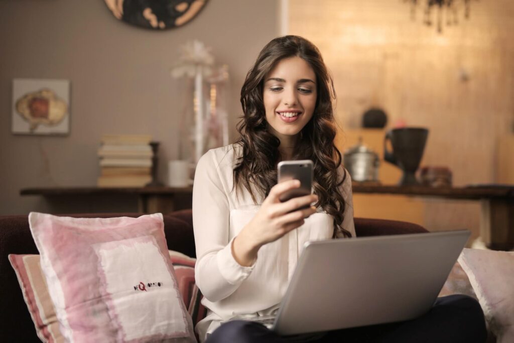 A woman looking at her phone while holding a laptop on her lap