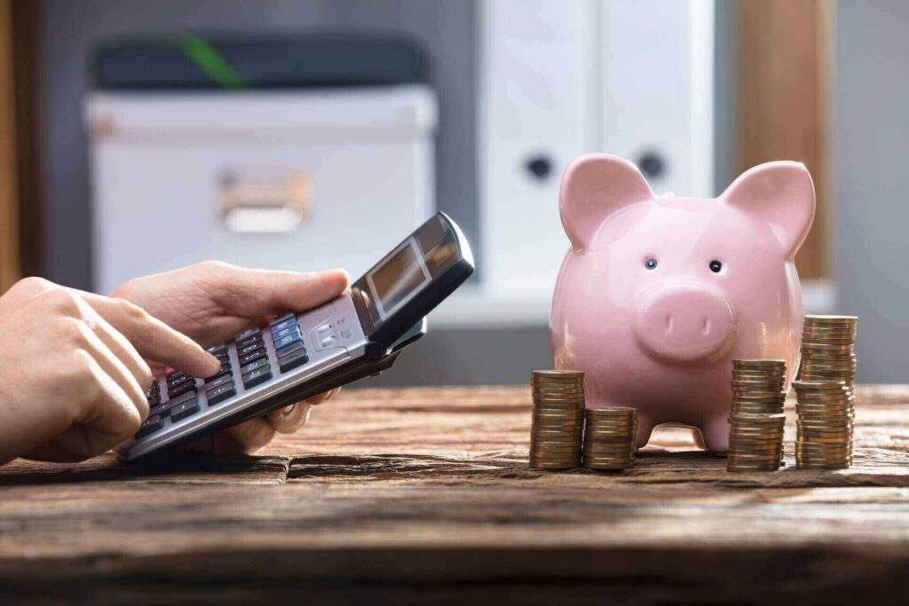 Person typing on a calculator with a piggy bank on the table next to them