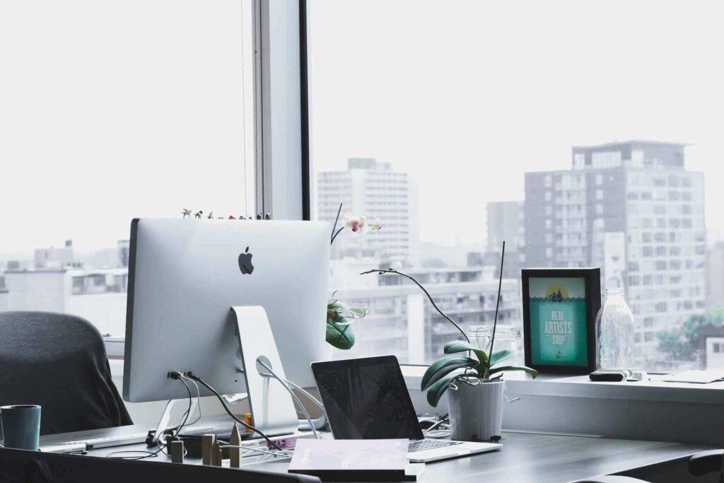 Office desk with a computer and a laptop on it and a big window behind it